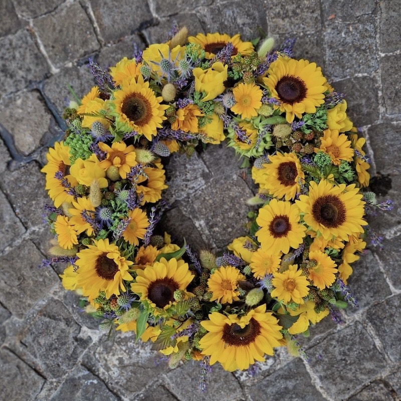 Kranz aus gelben Sonnenblumen und Lavendel auf Kopfsteinpflaster. Ideal für sommerliche Dekorationen.