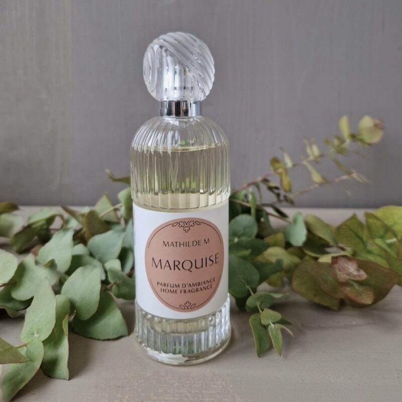 Parfumflasche „Marquise“ von Mathilde M., umgeben von Eucalyptusblättern auf einem Holztisch.