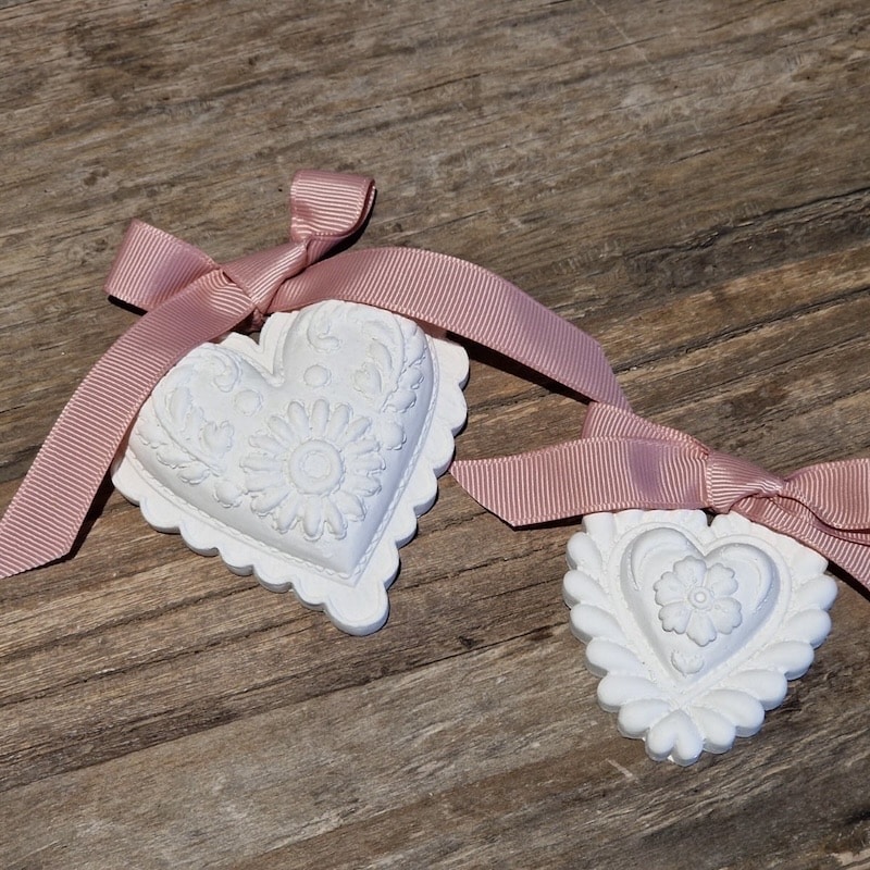 Weiße herzförmige Ornamente mit rosa Schleifen auf Holzuntergrund.