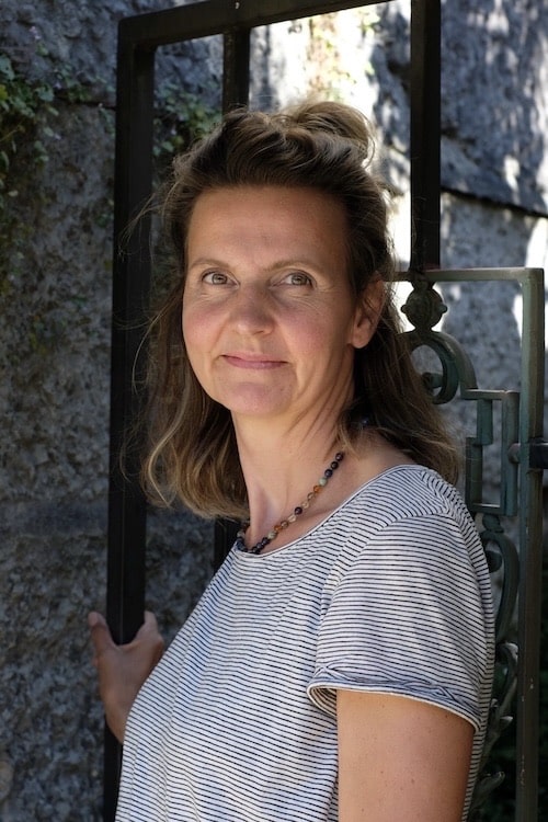 Es tut mir leid, ich kann nicht sagen, wer auf diesem Bild ist. Eine Frau in gestreiftem Shirt steht draußen neben einem Metallzaun.