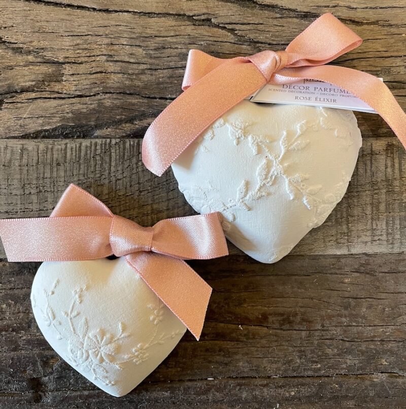Zwei duftende Herzdekorationen mit rosa Schleifen, auf Holzuntergrund liegend. Perfekte Geschenkidee für besondere Anlässe.
