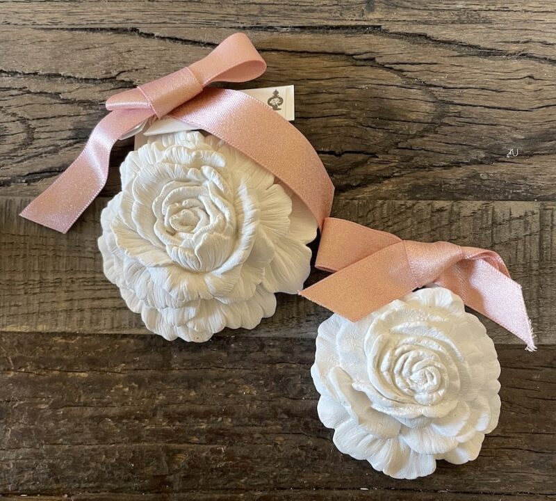 Weiße Blumen-Gießformen mit rosa Schleife auf Holzoberfläche. Elegante Deko für kreative Projekte und Handwerksideen.