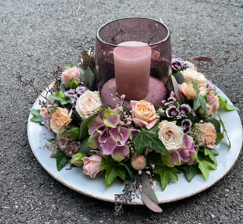 Romantisches Blumengesteck mit rosa Rosen und Kerze auf rustikalem Tablett für elegante Dekoration.