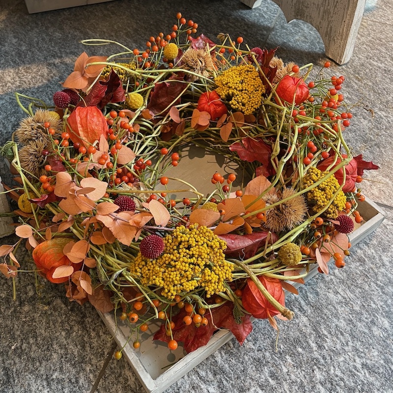 Herbstlicher Kranz mit bunten Beeren und Blättern auf Steinboden für herbstliche Dekoration, rustikales Design.