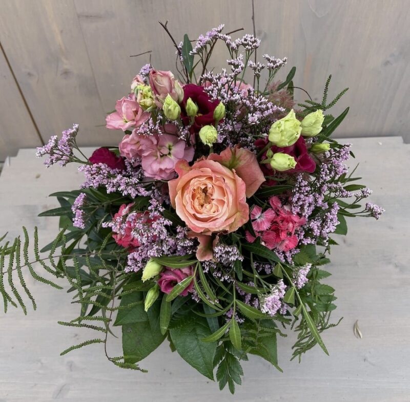 Bunter Blumenstrauß mit Rosen, Nelken und lila Blüten auf Holzhintergrund, ideal für Dekorationen und Geschenke.