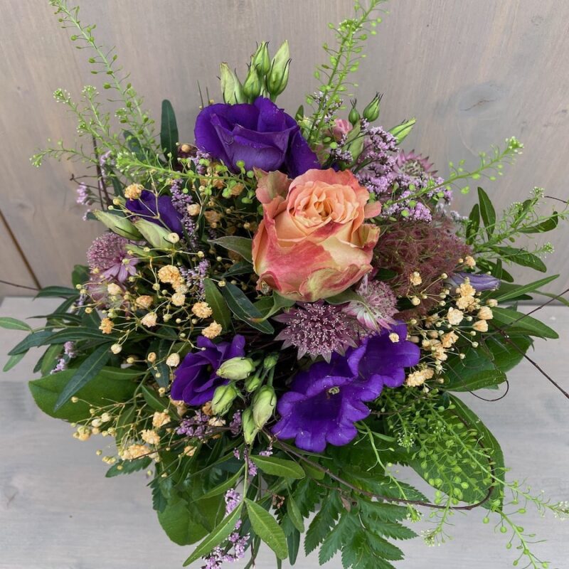 Bunter Blumenstrauß mit orangefarbener Rose und lila Blumen, umgeben von grünen Blättern auf hellem Hintergrund.