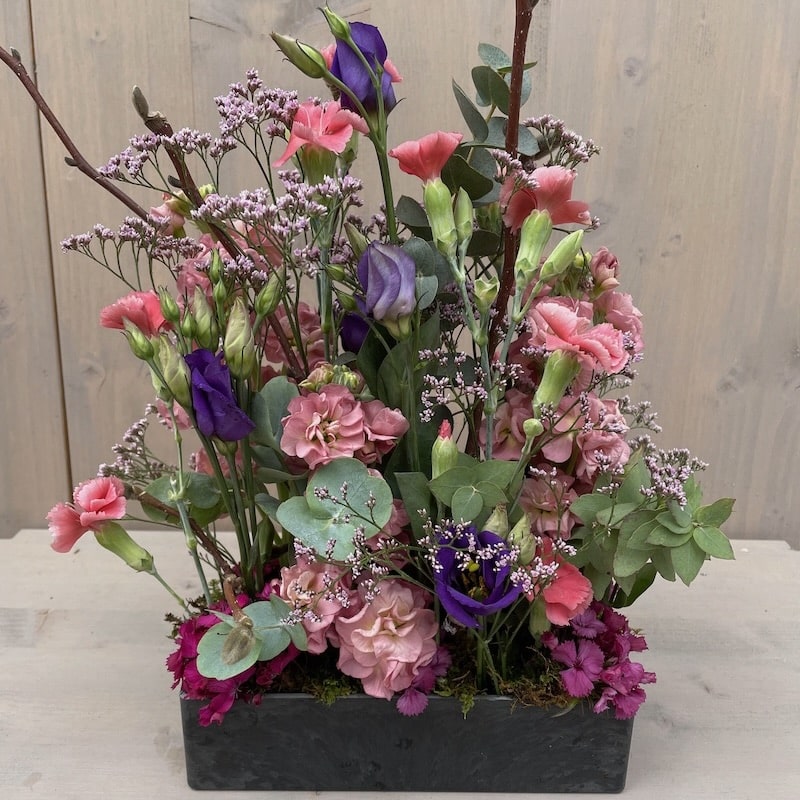 Gärtli in rechteckigem Gefäss mit rosa, lila und grünen Blüten vor hellem Holz.