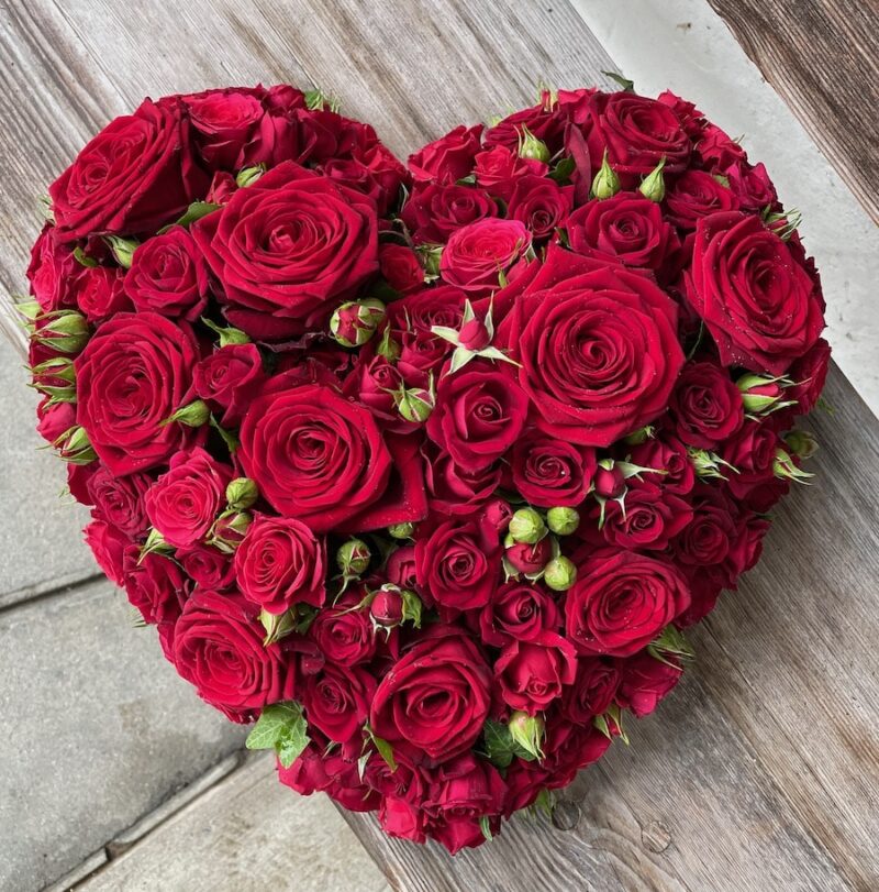 Herzförmiges Blumenarrangement aus roten Rosen auf Holzhintergrund, ideal für romantische Anlässe oder Hochzeiten.