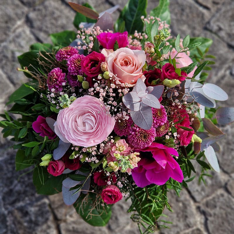 Bunter Blumenstrauß mit Rosen, Ranunkeln und Eukalyptus vor grauem Hintergrund. Perfekt für besondere Anlässe.
