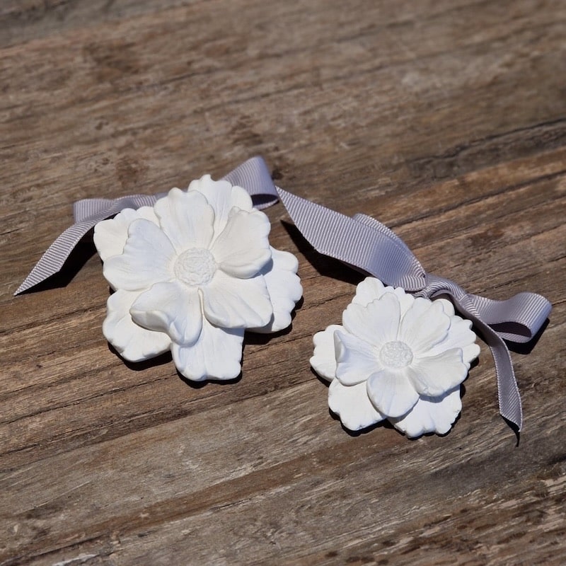 Weiße Gipsblumen mit Band auf Holztisch, dekorativ und handgemacht für kreative Deko-Ideen.