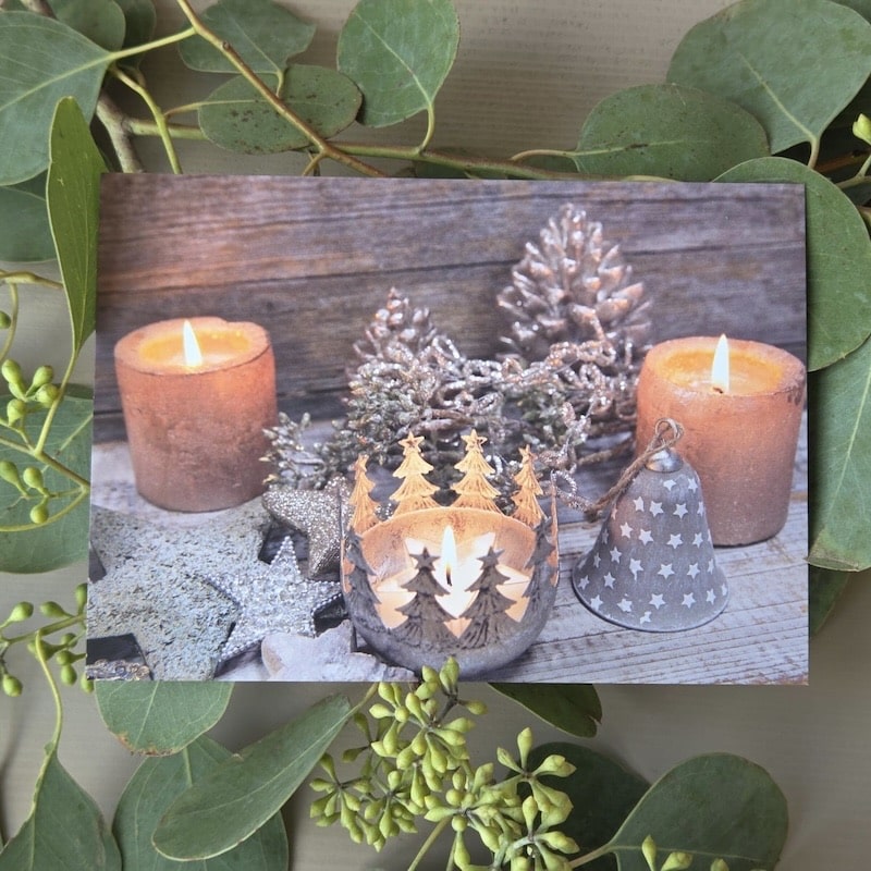 Weihnachtliche Kerzendekoration mit Tannenbaum- und Sternmotiven, umgeben von Grüntönen auf Holzuntergrund.