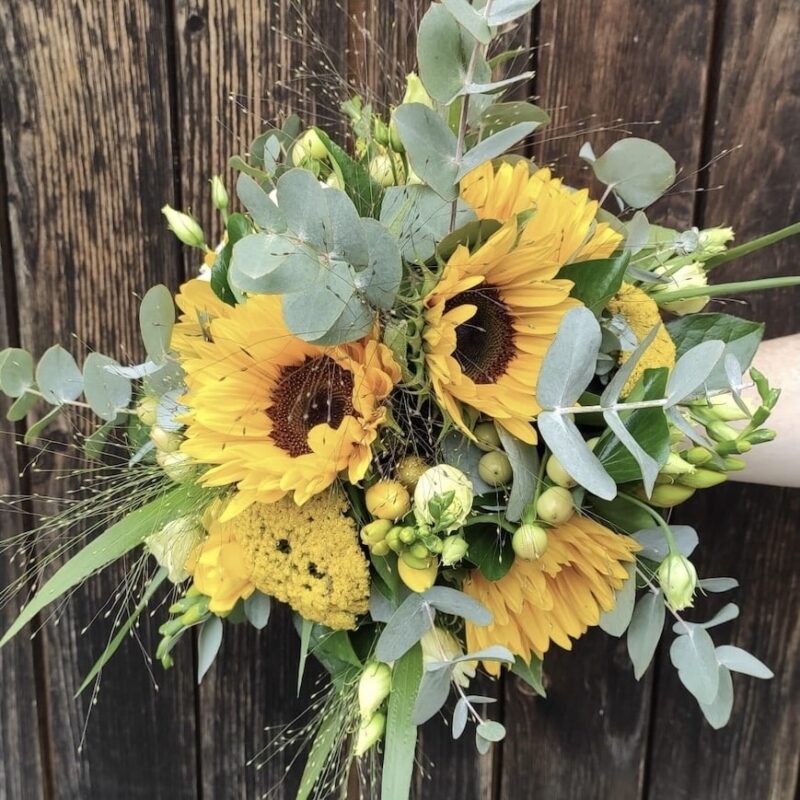 Strahlender Blumenstrauß mit Sonnenblumen und Eukalyptus vor Holzhintergrund. Ideal für sommerliche Dekoration.