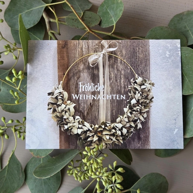 Weihnachtskranz mit Schleife auf Holz, umgeben von Eukalyptusblättern. Text: Fröhliche Weihnachten.