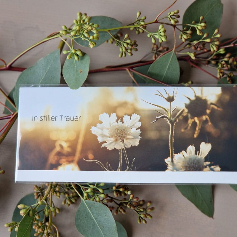 Trauerkarte mit Foto von Wildblumen bei Sonnenuntergang und Aufschrift In stiller Trauer, umrahmt von Eukalyptus.