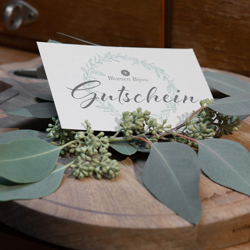 Gutschein von Blumen Bijou mit Eukalyptus-Dekoration auf Holztisch arrangiert.