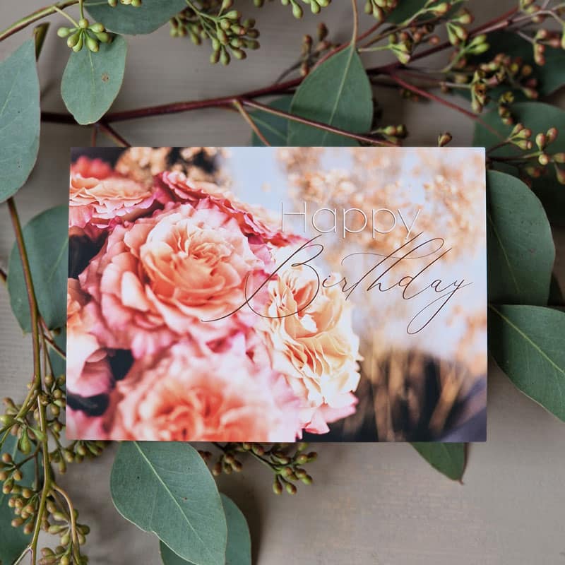 Geburtstagskarte mit rosa Rosen und der Aufschrift „Happy Birthday“, umgeben von grünen Blättern und Zweigen.