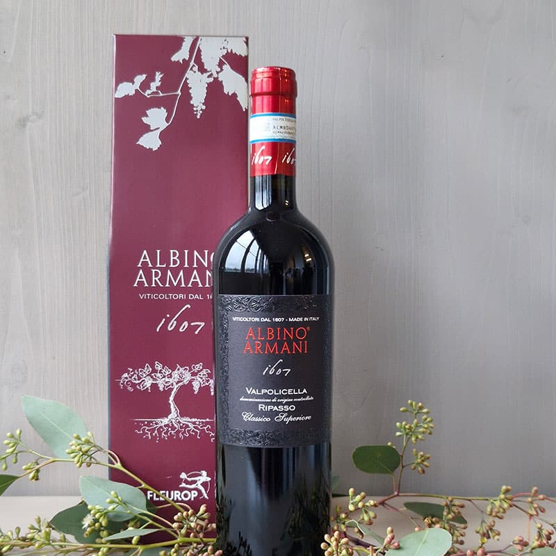 Flasche Albino Armani Valpolicella Ripasso Wein mit rotem Geschenkkarton, dekoriert mit grünen Zweigen.